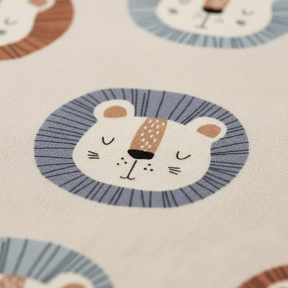 Macro view of textile printed with a repeating cartoon lion face pattern in blue, brown, and beige.