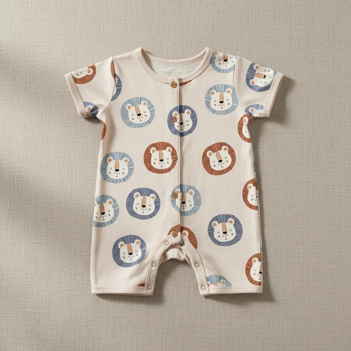 Short-sleeve baby romper featuring an all-over print of cartoon lion faces against a neutral cream background.