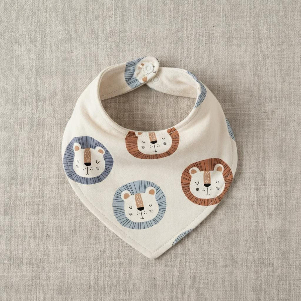 Triangular baby bib made of cream-colored fabric with a repeating pattern of stylized lion faces.