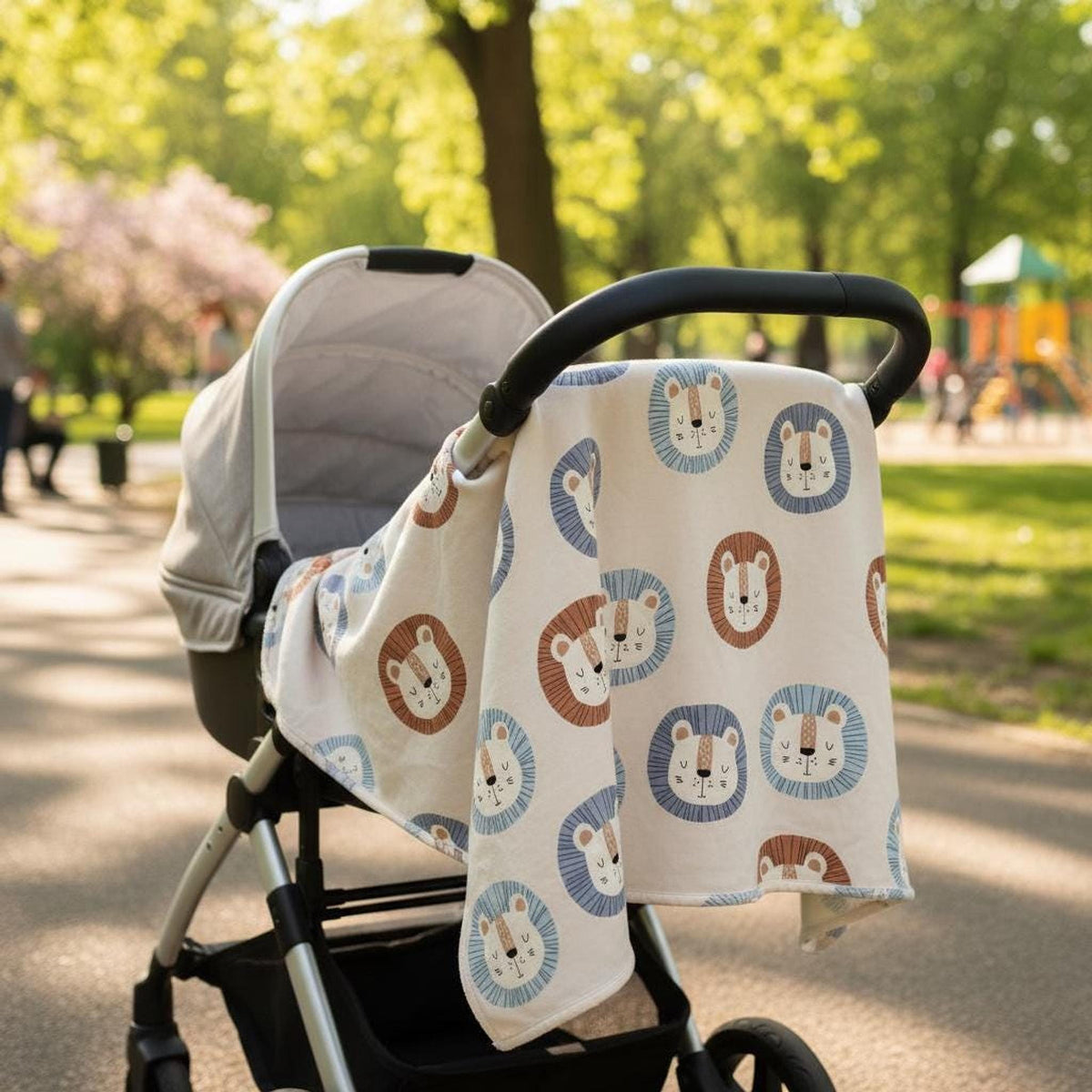 Stroller in a sunny park with a patterned baby blanket featuring cartoon lion faces draped over the handlebar.