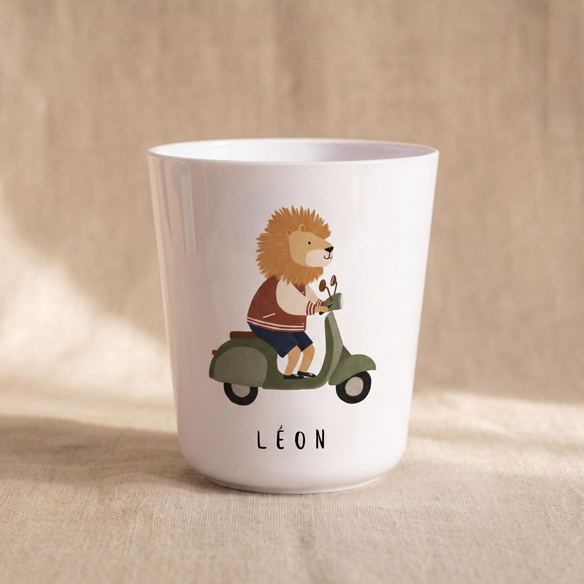 A white polymer cup featuring a lion wearing a jacket and riding a green scooter, with the name Leon printed below.