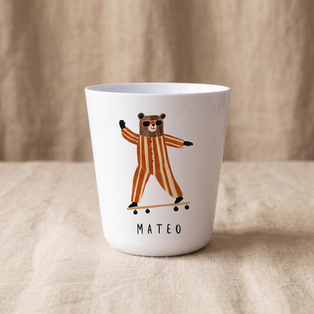 A white polymer cup showing a bear wearing sunglasses and striped pajamas while riding a skateboard, with the name Mateo printed below.