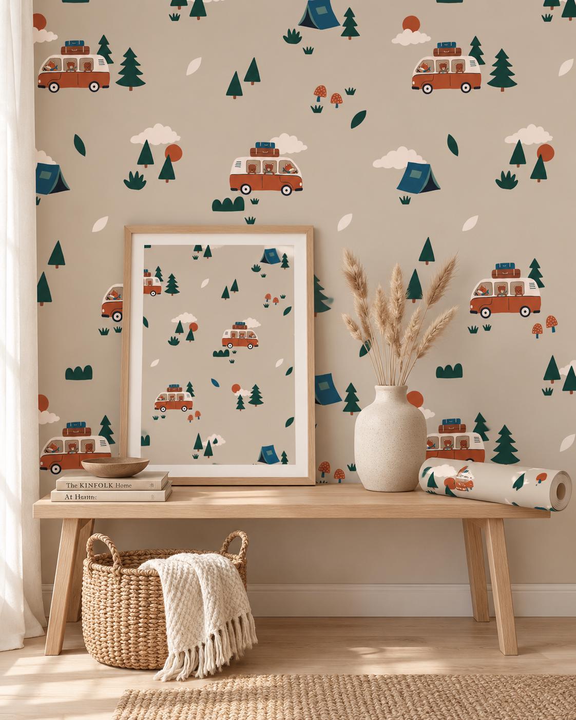 Wallpaper featuring a repeating pattern of orange camper vans with luggage on top, blue tents, dark green pine trees, red suns, white clouds, and small mushrooms on a light beige background. The design is displayed on a wall and in a frame.