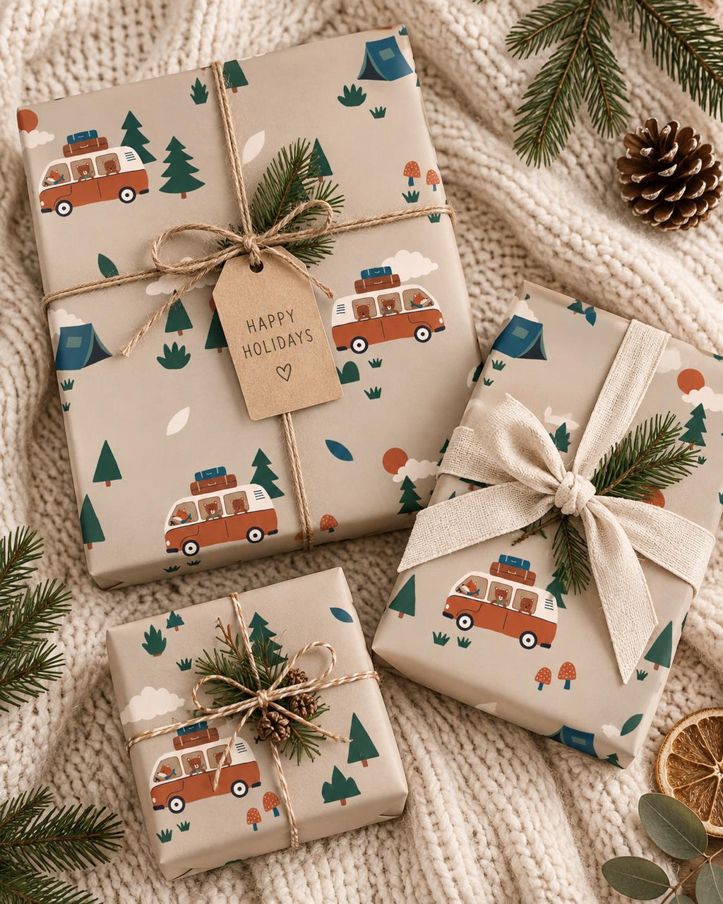 Three rectangular gifts wrapped in beige paper featuring a repeating pattern of orange camper vans, green pine trees, blue tents, and red mushrooms. The gifts are tied with twine or ribbon and decorated with small pine sprigs and a gift tag.
