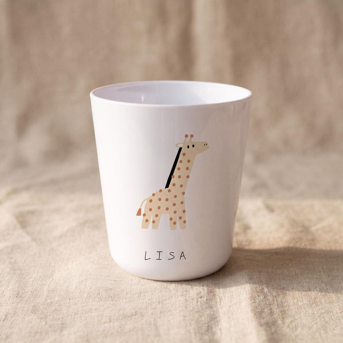 A white cup featuring a tan giraffe illustration with brown spots and a black mane. The name LISA is printed in black capital letters below the giraffe. The cup has a smooth, glossy finish and a slightly tapered cylindrical shape.