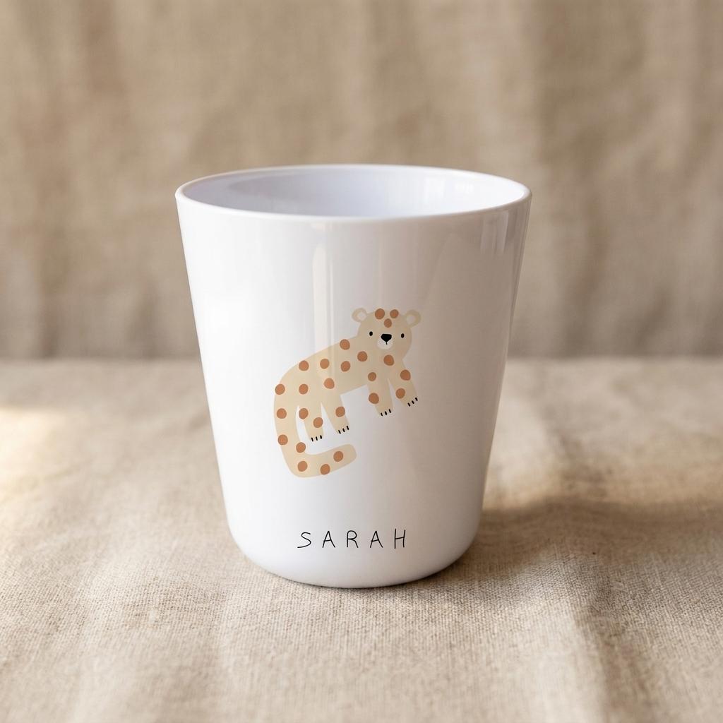 A white tumbler featuring a light brown leopard illustration with darker brown spots. The name SARAH is printed in simple black capital letters below the leopard graphic. The cup has a smooth, glossy finish and a tapered cylindrical shape.