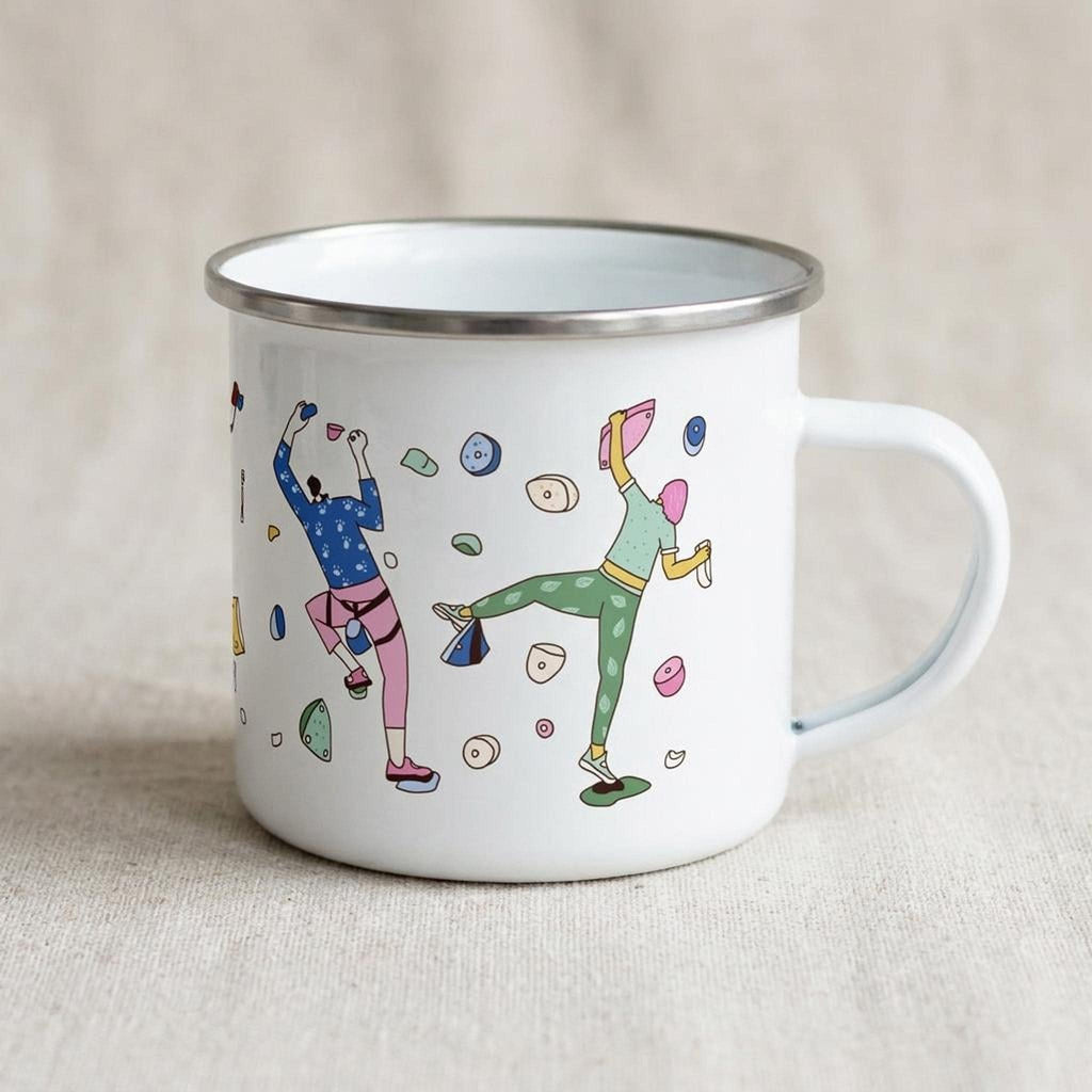A white enamel mug featuring a climber design rests on a neutral surface.