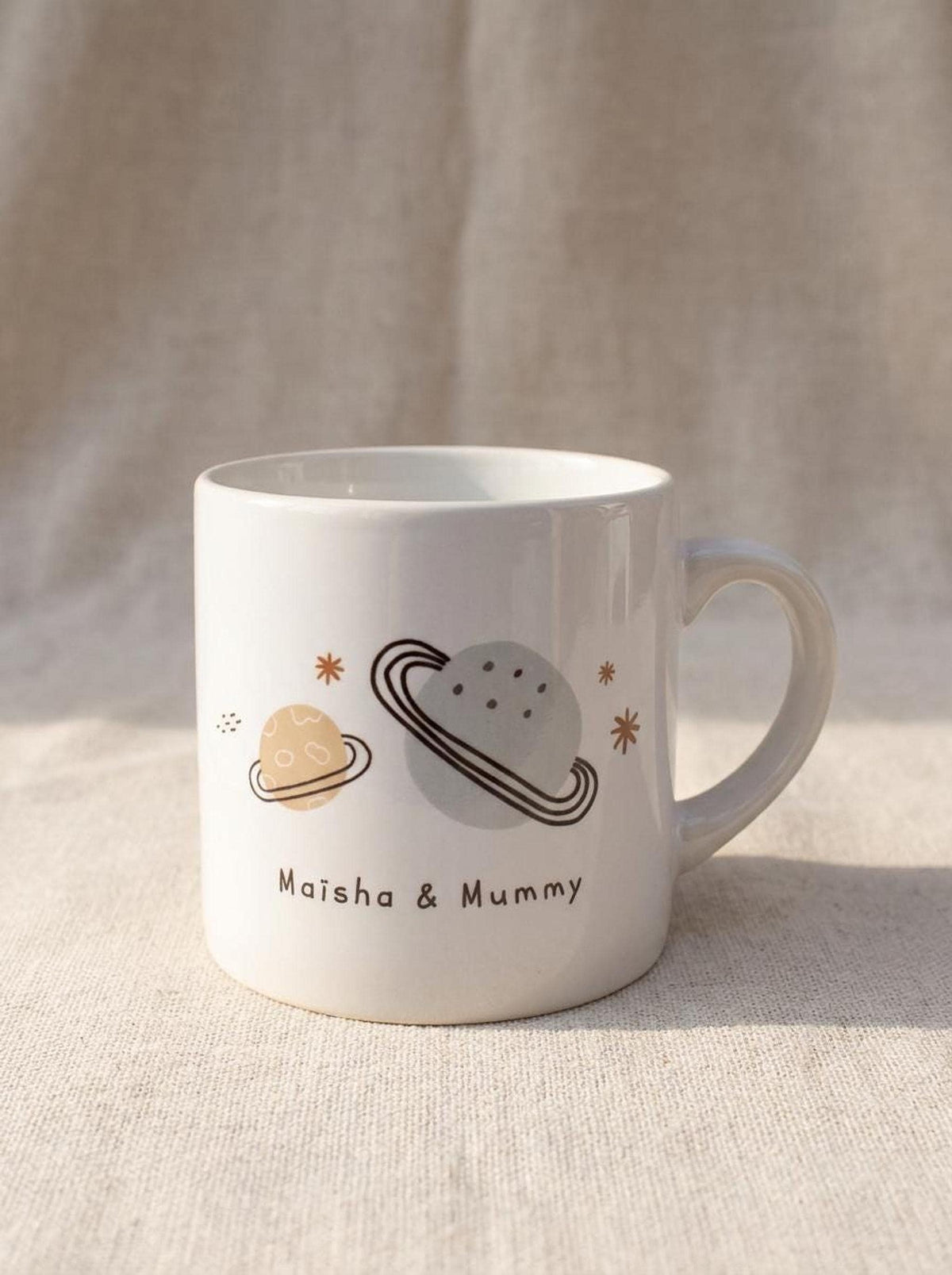 A single smaller white ceramic mug features illustrations of planets and the text Maisha & Mummy.