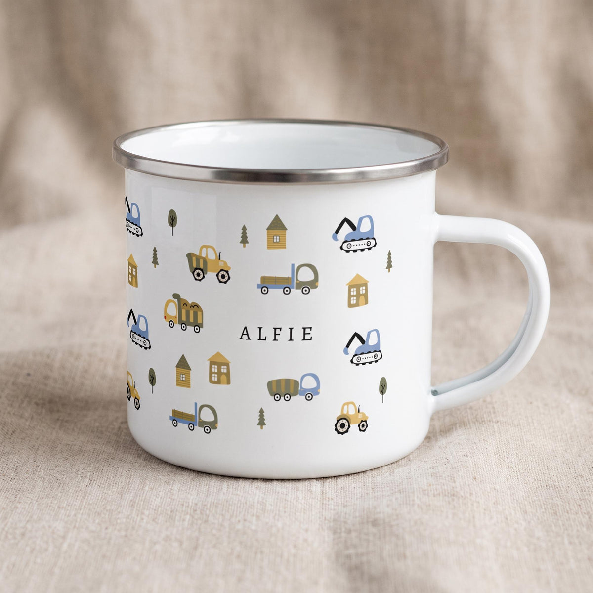 A white enamel mug with a silver rim displays a pattern of construction vehicles and trees with the name ALFIE printed in black on the side.