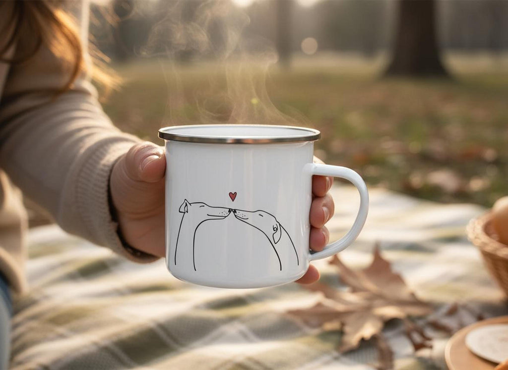 A hand holds a steaming white enamel mug outdoors with a line drawing of two dogs kissing under a red heart.