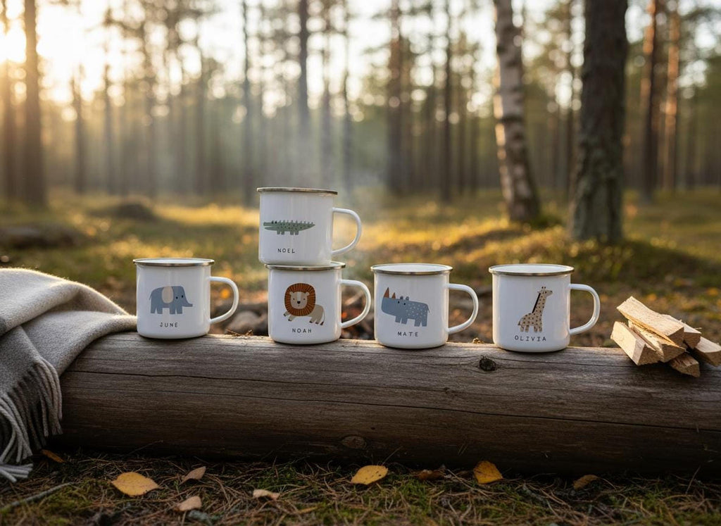 A stack of five personalised safari animal enamel mugs resting on a fallen log in a sunlit forest.