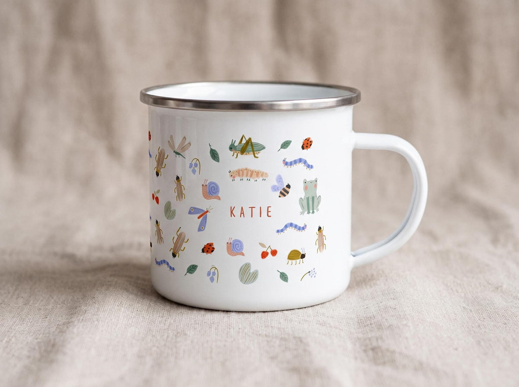 White enamel mug decorated with various insect illustrations and the custom name KATIE on the side.