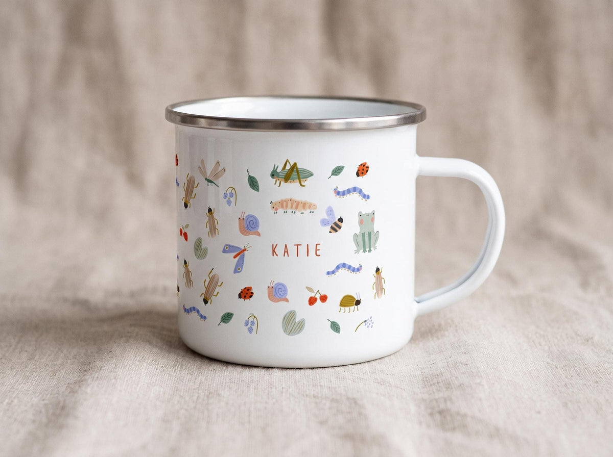 White enamel mug decorated with various insect illustrations and the custom name KATIE on the side.