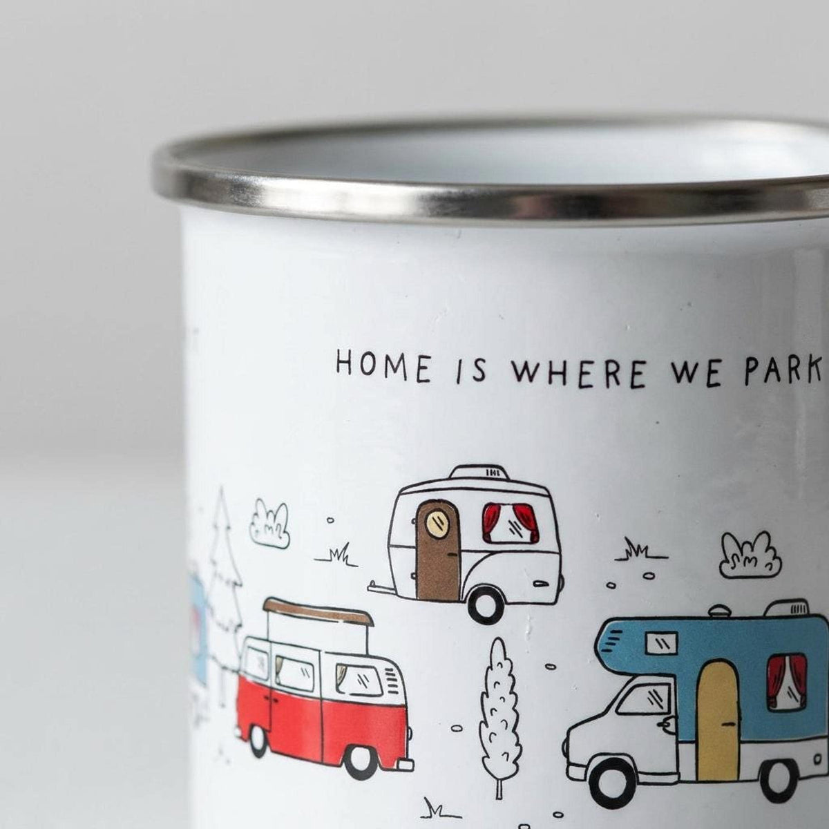 Close-up of the text HOME IS WHERE WE PARK IT and campervan illustrations on the white enamel mug.