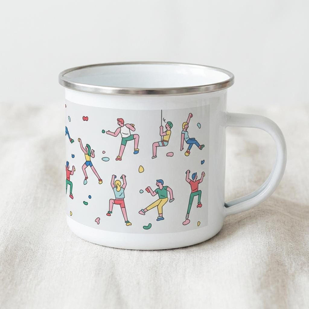 A white enamel mug with a silver rim and handle stands on a light fabric surface, featuring a wrap-around illustration of rock climbers.