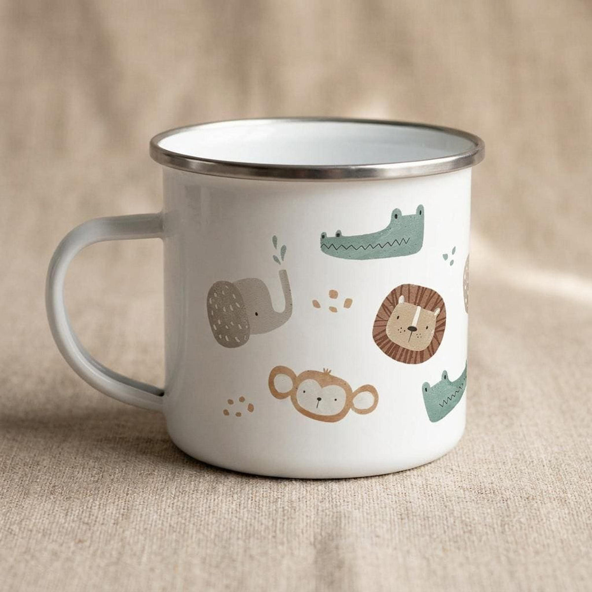 A white enamel mug with a silver rim and handle is displayed on a textured beige surface, showing safari animal illustrations.