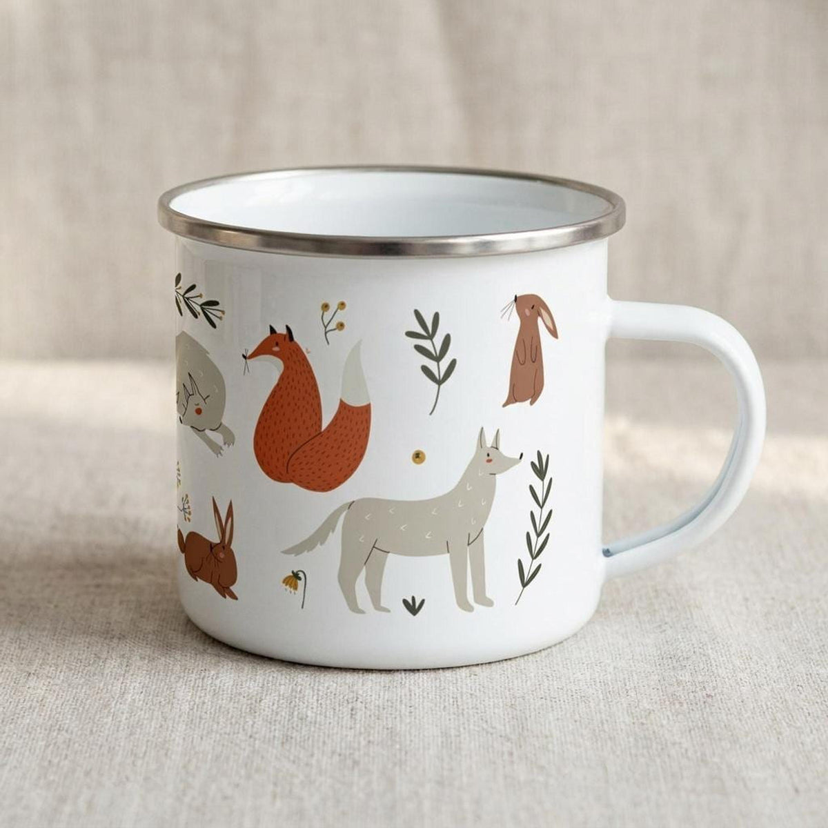 A white enamel mug with a silver rim displays woodland creatures including a standing gray wolf, a sitting red fox, and brown rabbits against a textured background.