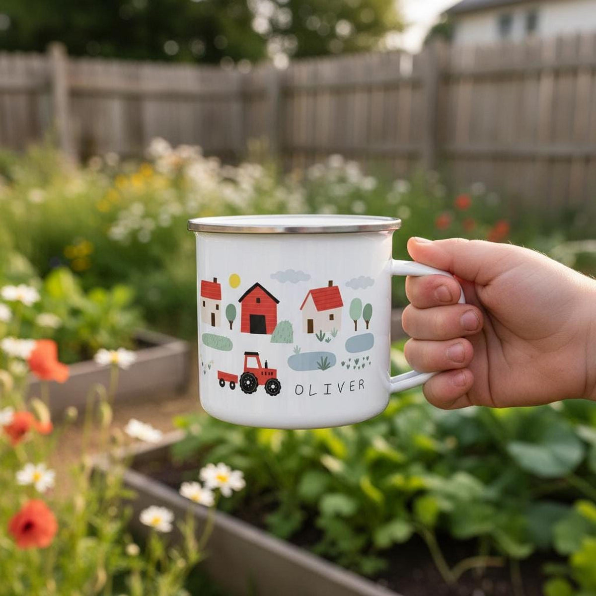 A hand holds a white enamel mug with a farm illustration and the name OLIVER in an outdoor garden.