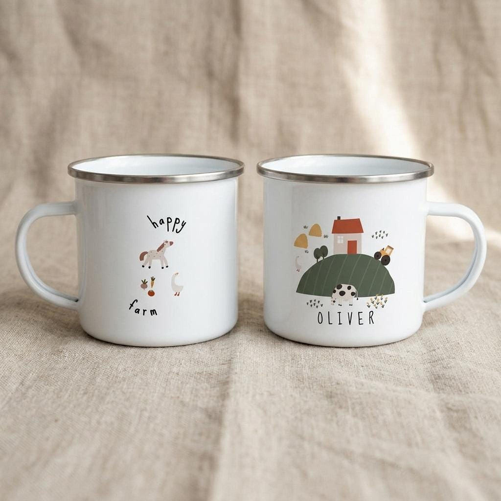 Two white enamel mugs sit side-by-side on a neutral fabric, one showing a happy farm illustration and the other a cartoon hill with the name Oliver.