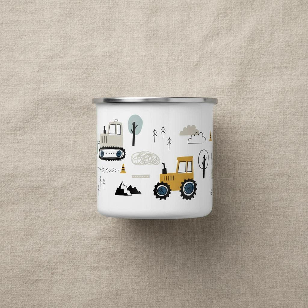 A white enamel mug with illustrations of construction vehicles and trees is centered on a light beige fabric backdrop.