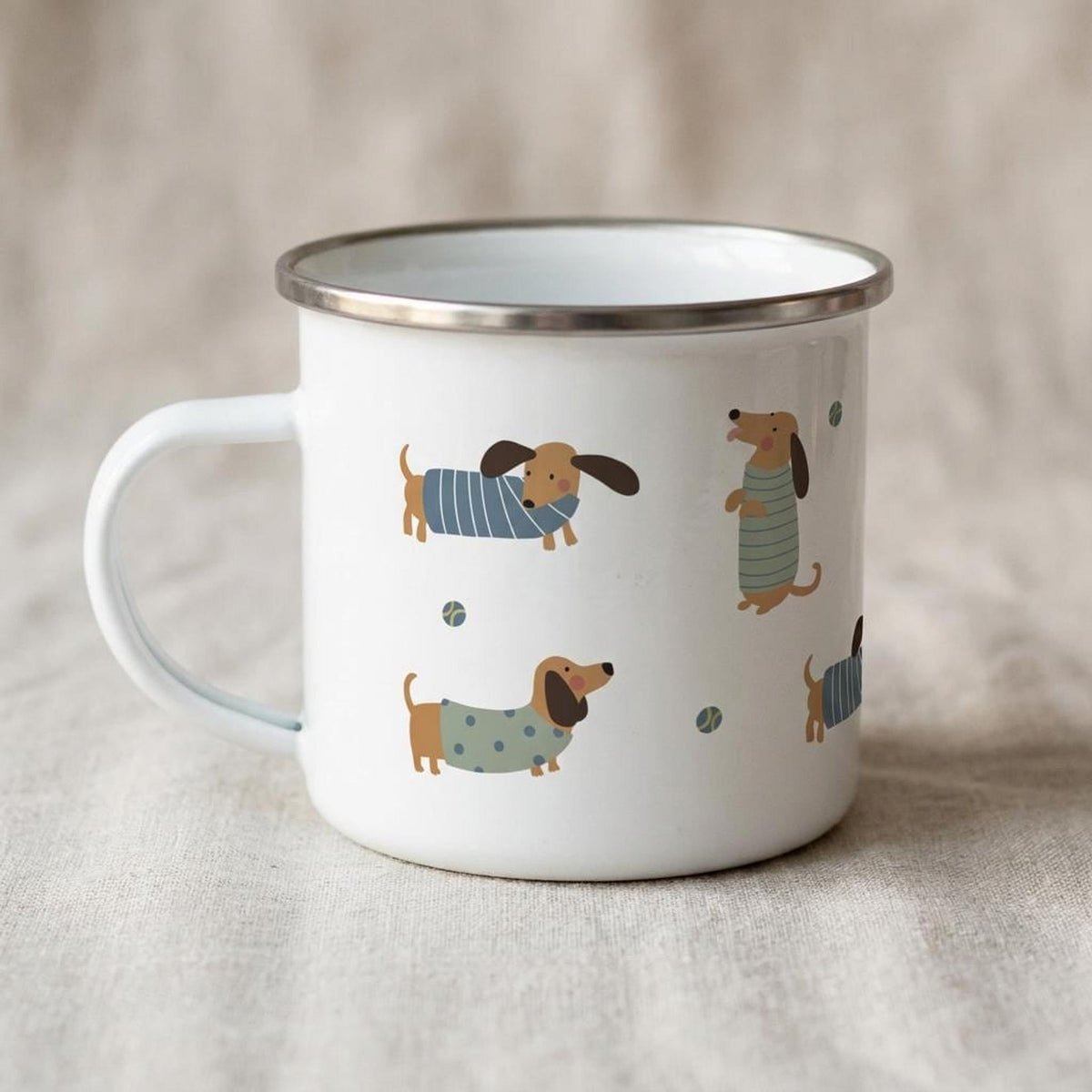 Another angle of the white enamel mug focusing on the handle and the illustrated dachshunds.