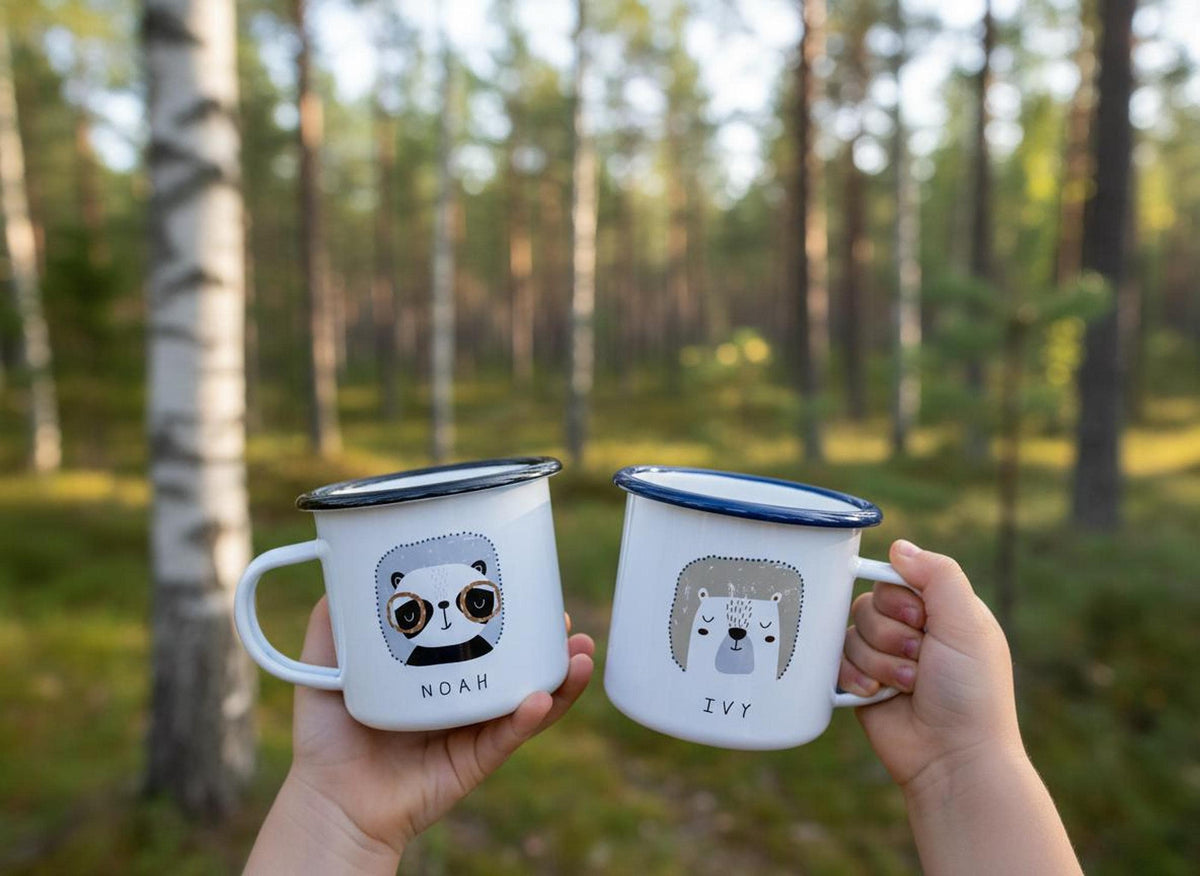 Hands hold up two white enamel animal-themed mugs against a blurred backdrop of trees.