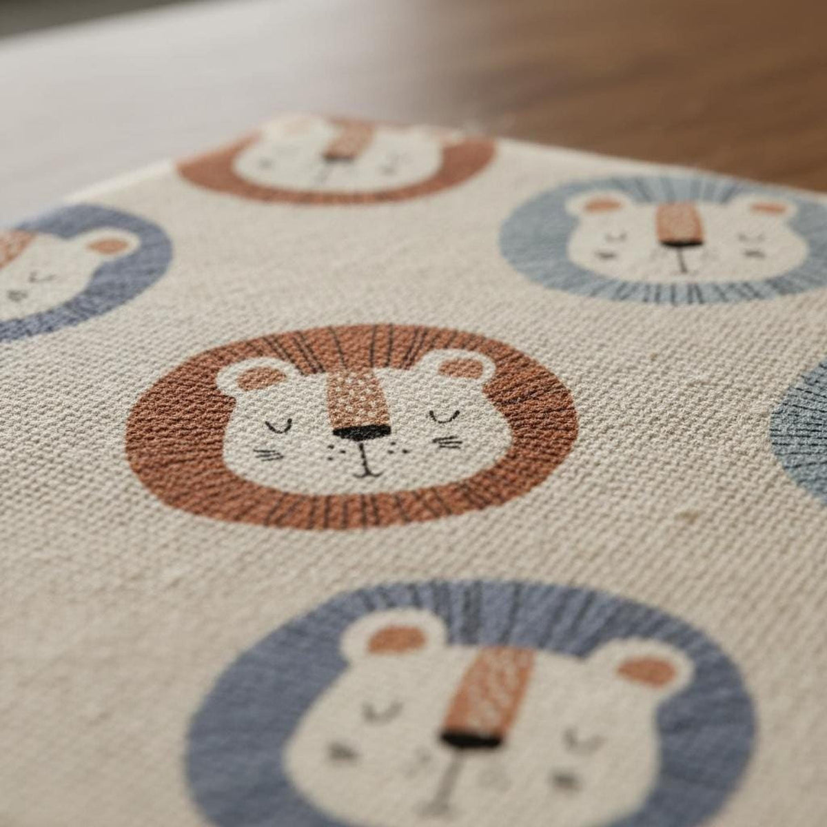 Close-up of woven fabric surface displaying a repeating lion face design in brown, blue, and cream tones.
