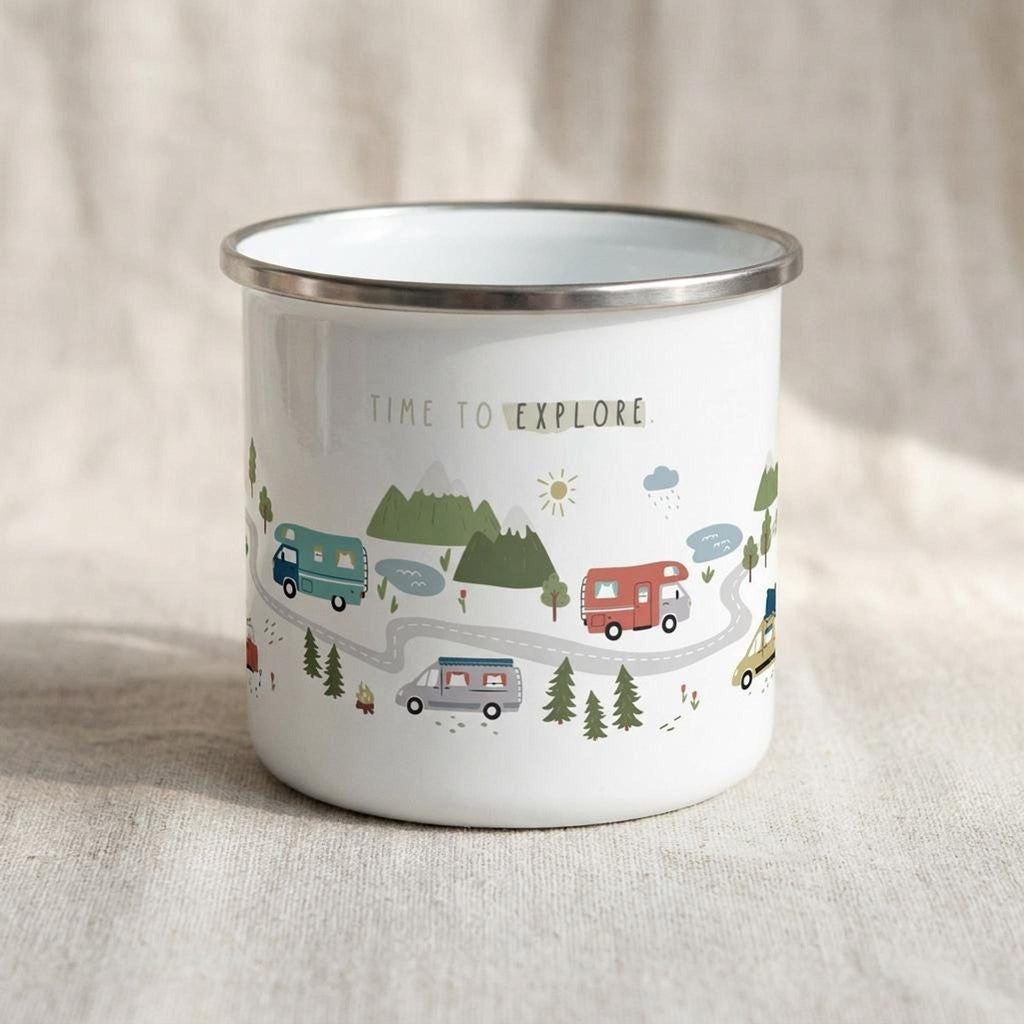 A white enamel camp mug with a silver rim displays a playful illustration of camper vans on a winding road with mountains, trees, and the text TIME TO EXPLORE, resting on a textured linen surface.
