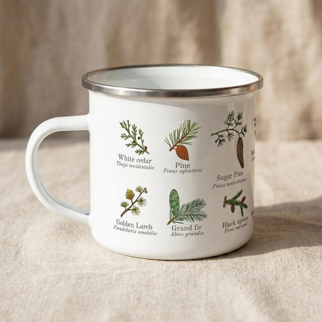 A white enamel camping mug with a silver rim displays botanical drawings and labels of conifer trees on a neutral cloth surface.