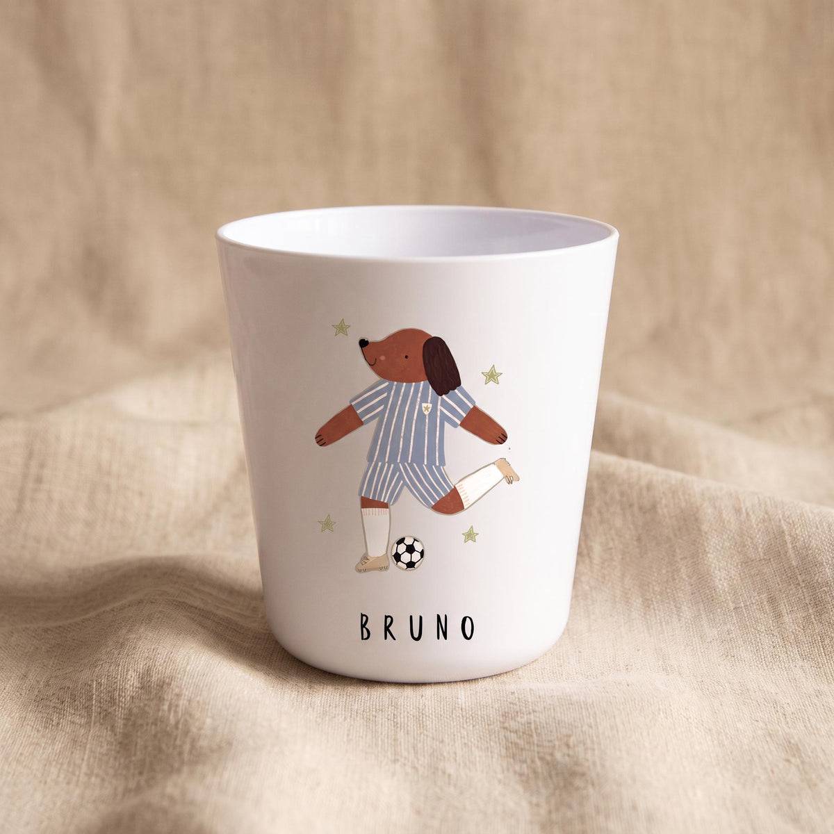 A white polymer cup with an illustration of a brown dog playing soccer next to a football, with the name Bruno printed below.