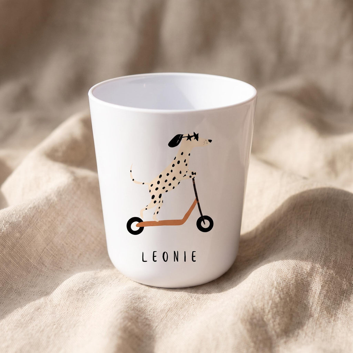 A white polymer cup featuring a dalmatian riding an orange scooter, with the name Leonie printed underneath.