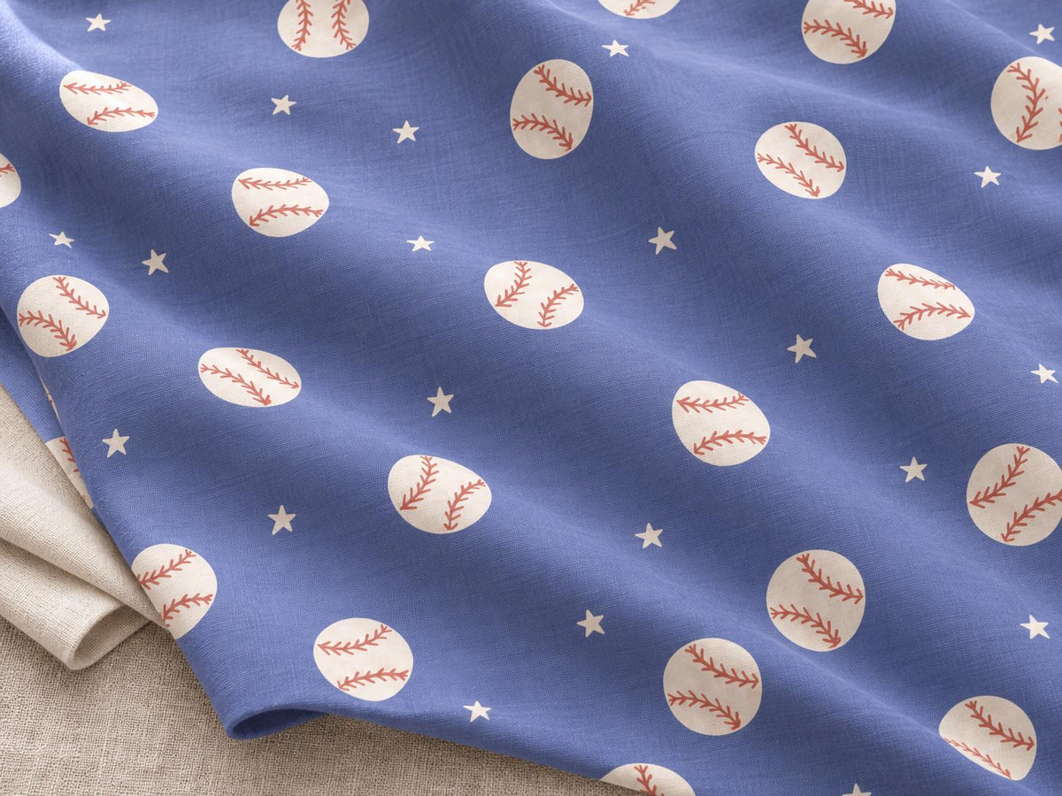A blue fabric featuring a repeating pattern of white baseballs with red stitching and small white stars scattered throughout. The material has a visible woven texture and is folded to show a plain light beige fabric underneath.
