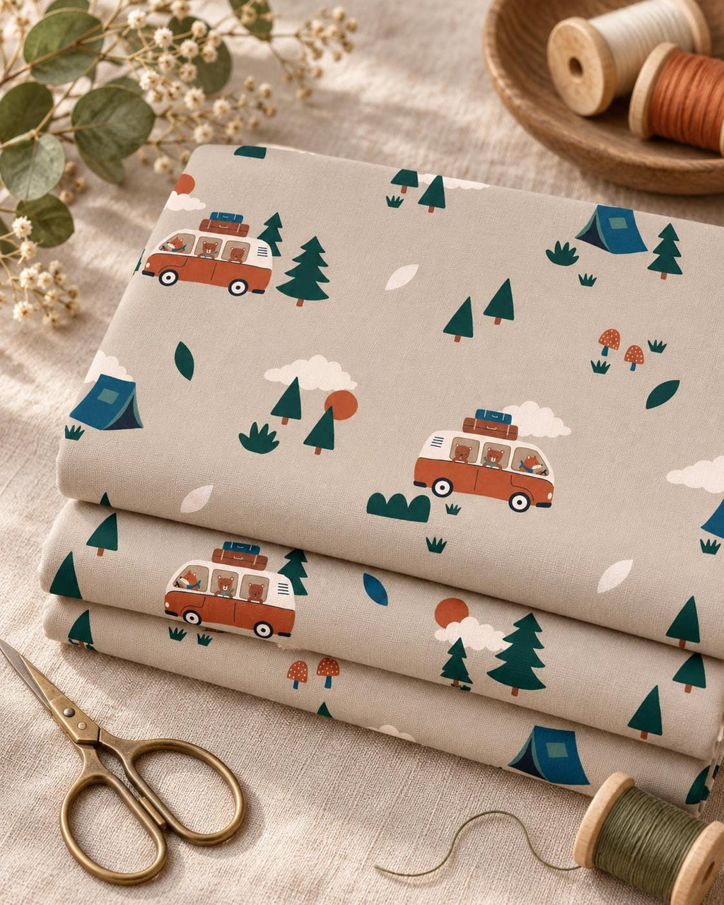 A stack of folded light grey fabric featuring a repeating pattern of orange camper vans with brown bears, dark green pine trees, blue tents, white clouds, orange suns, and small red mushrooms. The fabric has a smooth, matte texture.