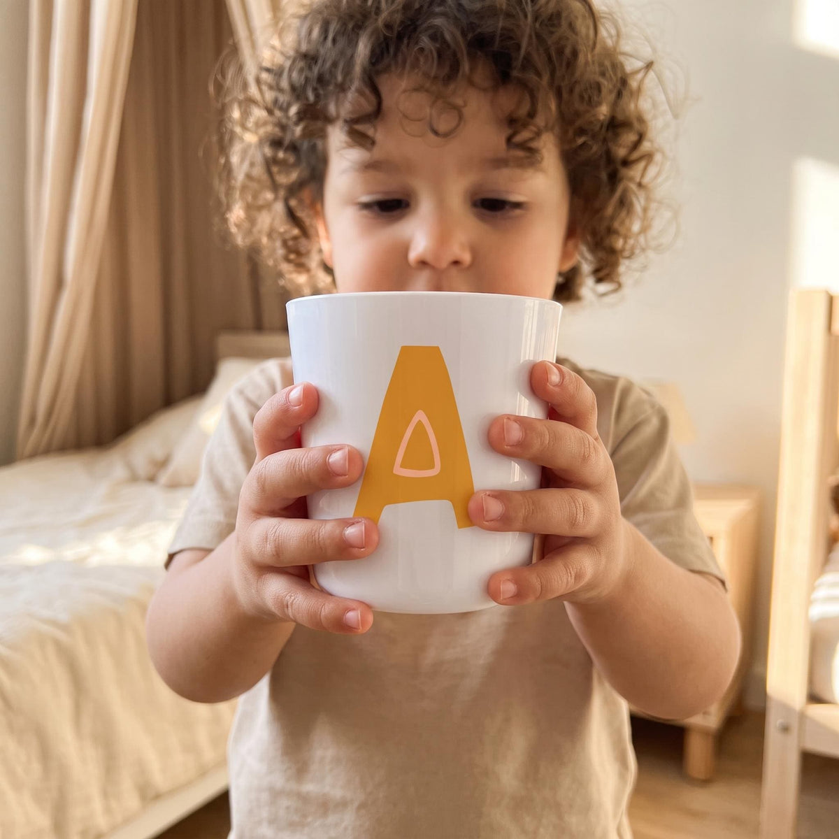 Personalised initial cup for toddlers displayed in a warm Scandinavian children's setting with playful colourful alphabet design.