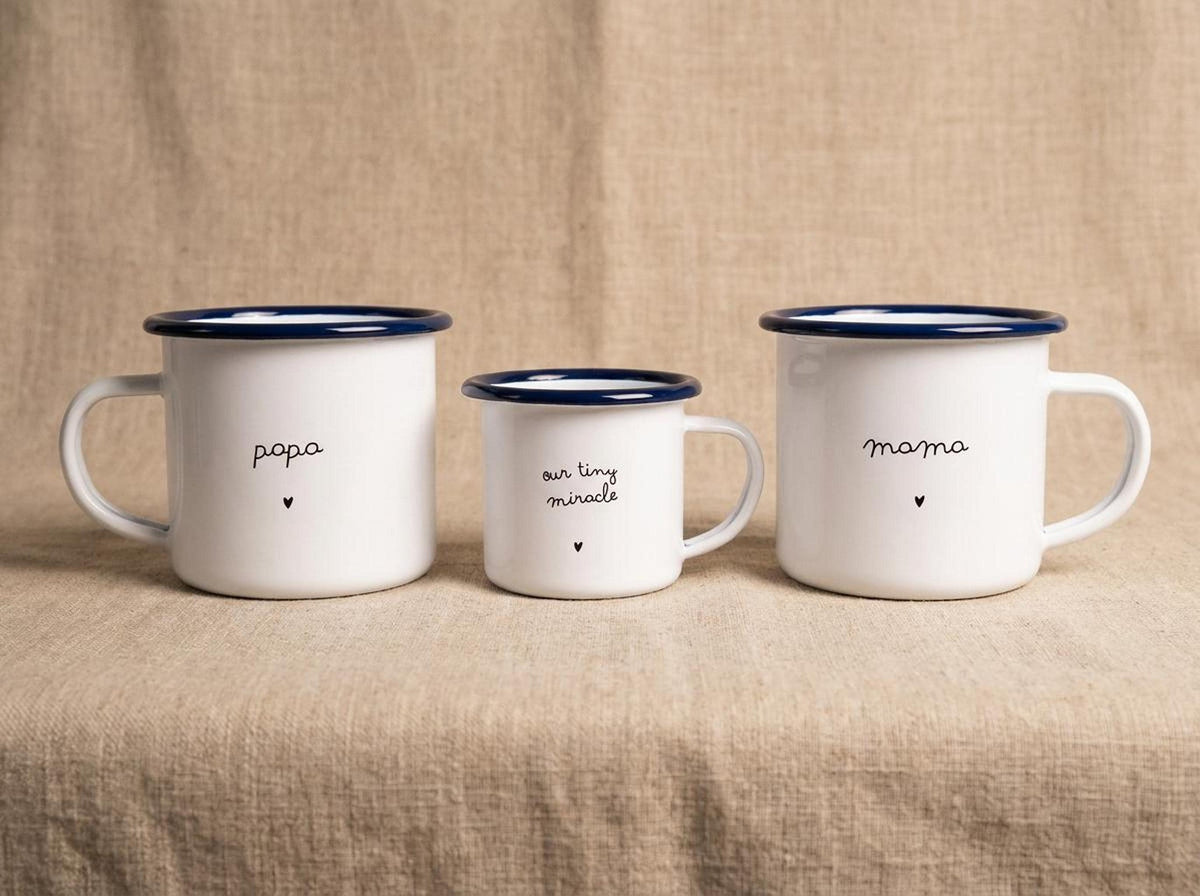 Three white enamel mugs with blue rims arranged with papa on the left, our tiny miracle in the middle, and mama on the right.