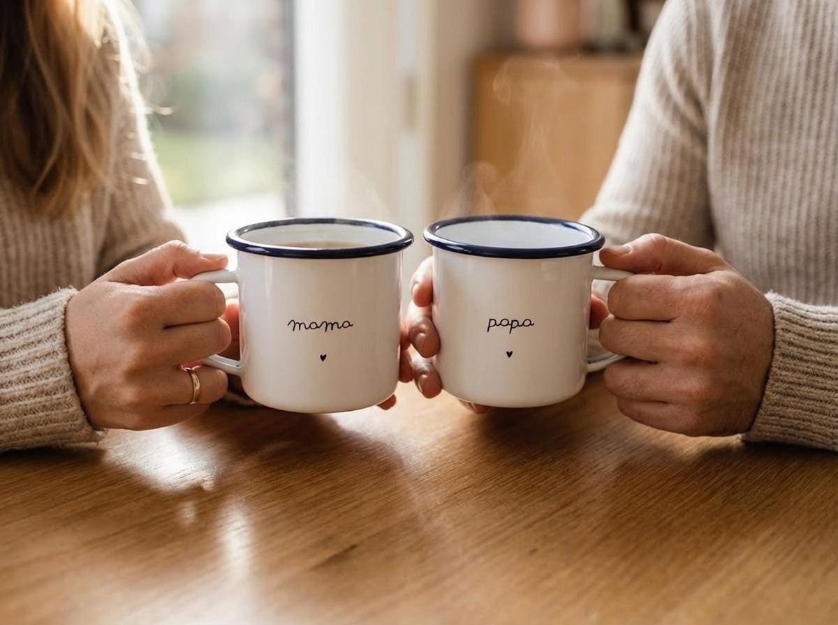 A man and a woman sitting at a wooden table holding steaming white enamel mugs labeled mama and papa.