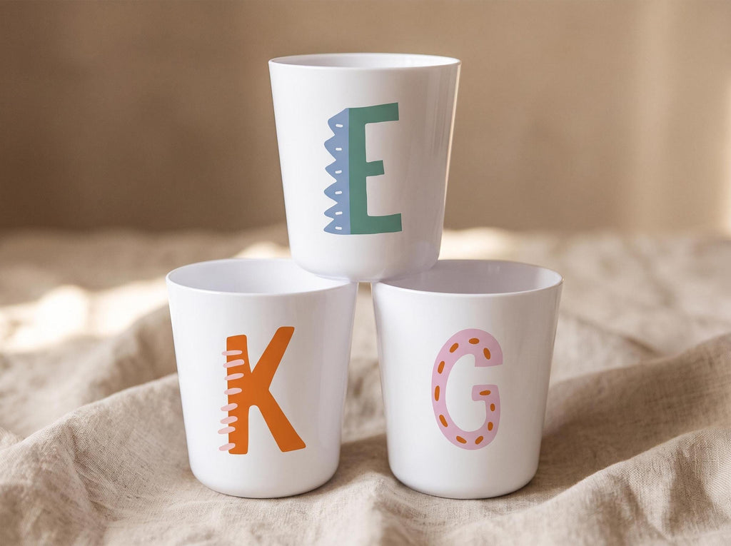 White personalised kids cup with a colourful illustrated initial letter, lightweight handleless plastic cup for toddlers.