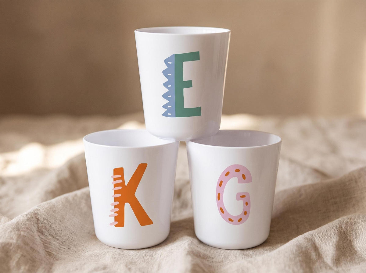 White personalised kids cup with a colourful illustrated initial letter, lightweight handleless plastic cup for toddlers.