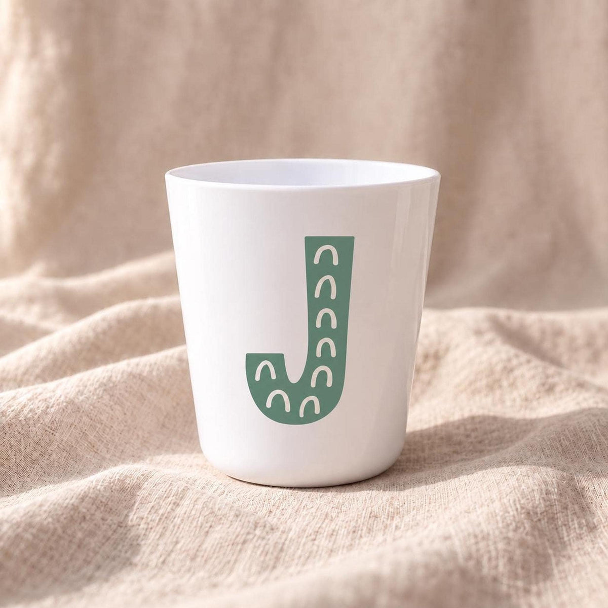 Close-up of personalised children's cup with large colourful illustrated initial printed on a white handleless plastic cup.