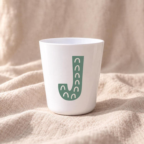 Close-up of personalised children's cup with large colourful illustrated initial printed on a white handleless plastic cup.