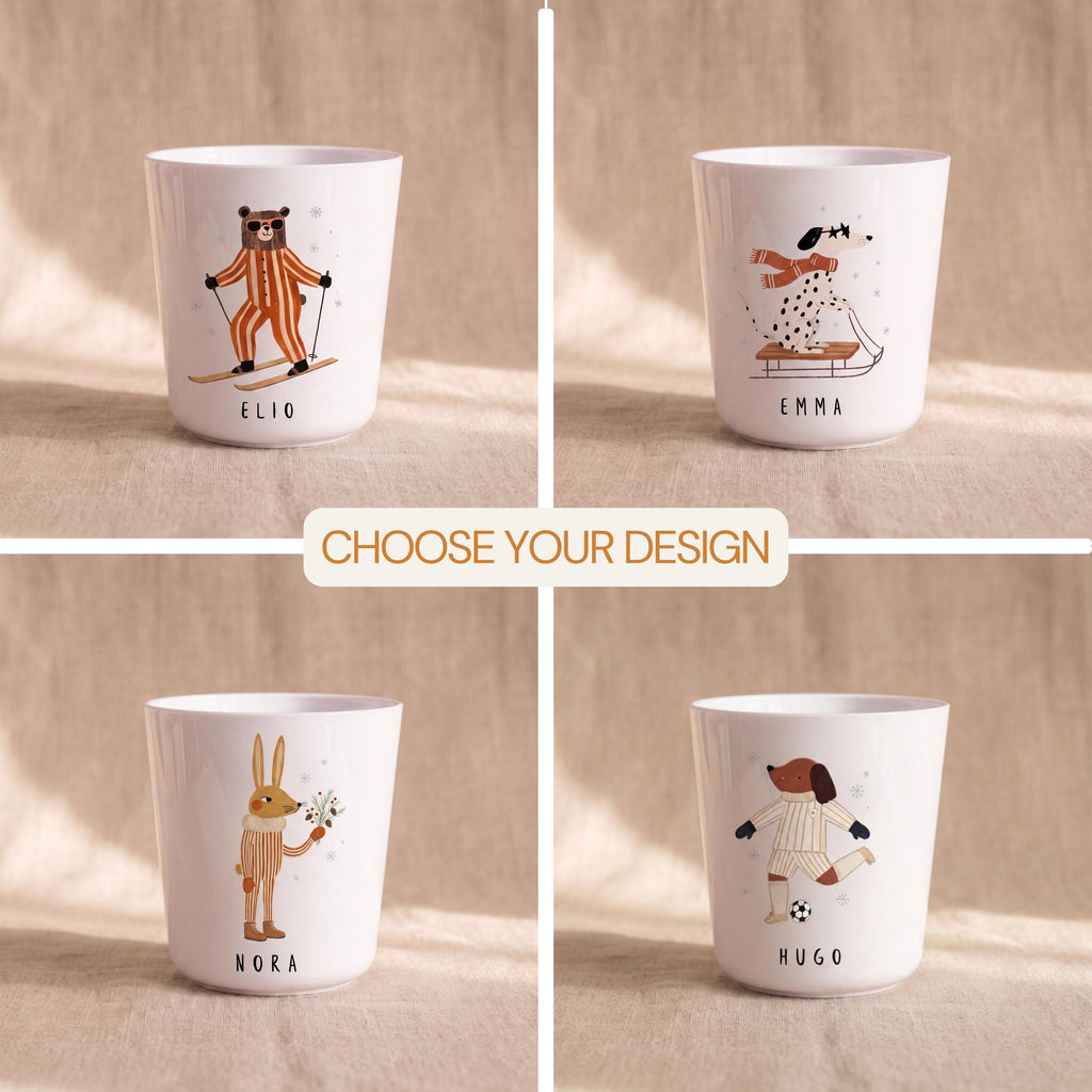 A four-panel grid showing different white children's cups with illustrations of a bear skiing, a dalmatian on a sled, a rabbit holding pine sprigs, and a dog playing soccer.