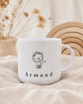 The white personalized kids mug with a lion graphic and the name Armand sits on draped fabric with dried florals in the background.
