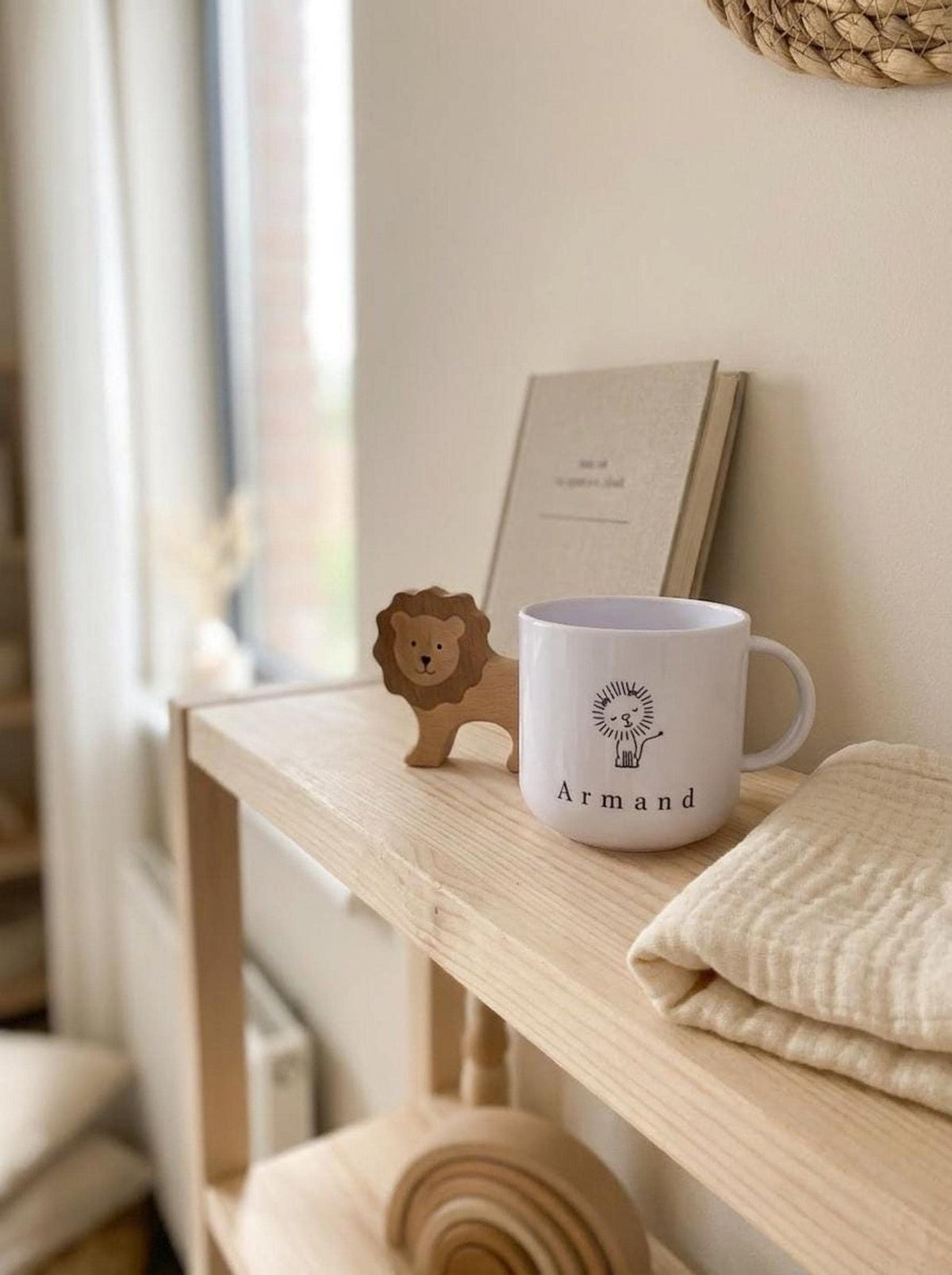 A wooden shelf displays the personalized white cup with a lion design alongside a small wooden lion figurine and a notebook.