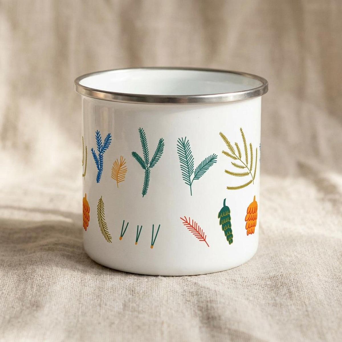 Front view of the white enamel mug showing a different assortment of colorful pine and cone motifs.