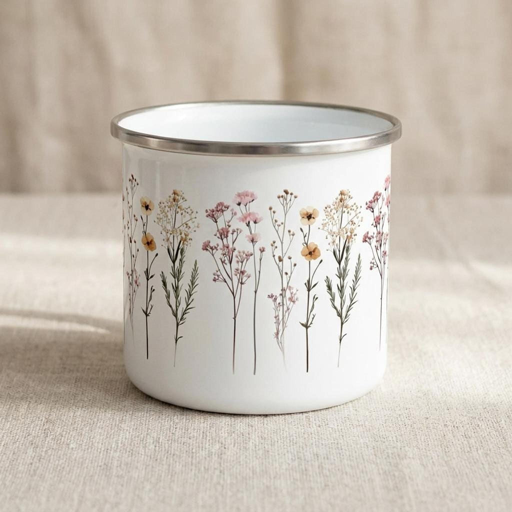 The white enamel mug is shown from another angle, displaying the repeating meadow flower graphic against the neutral fabric backdrop.