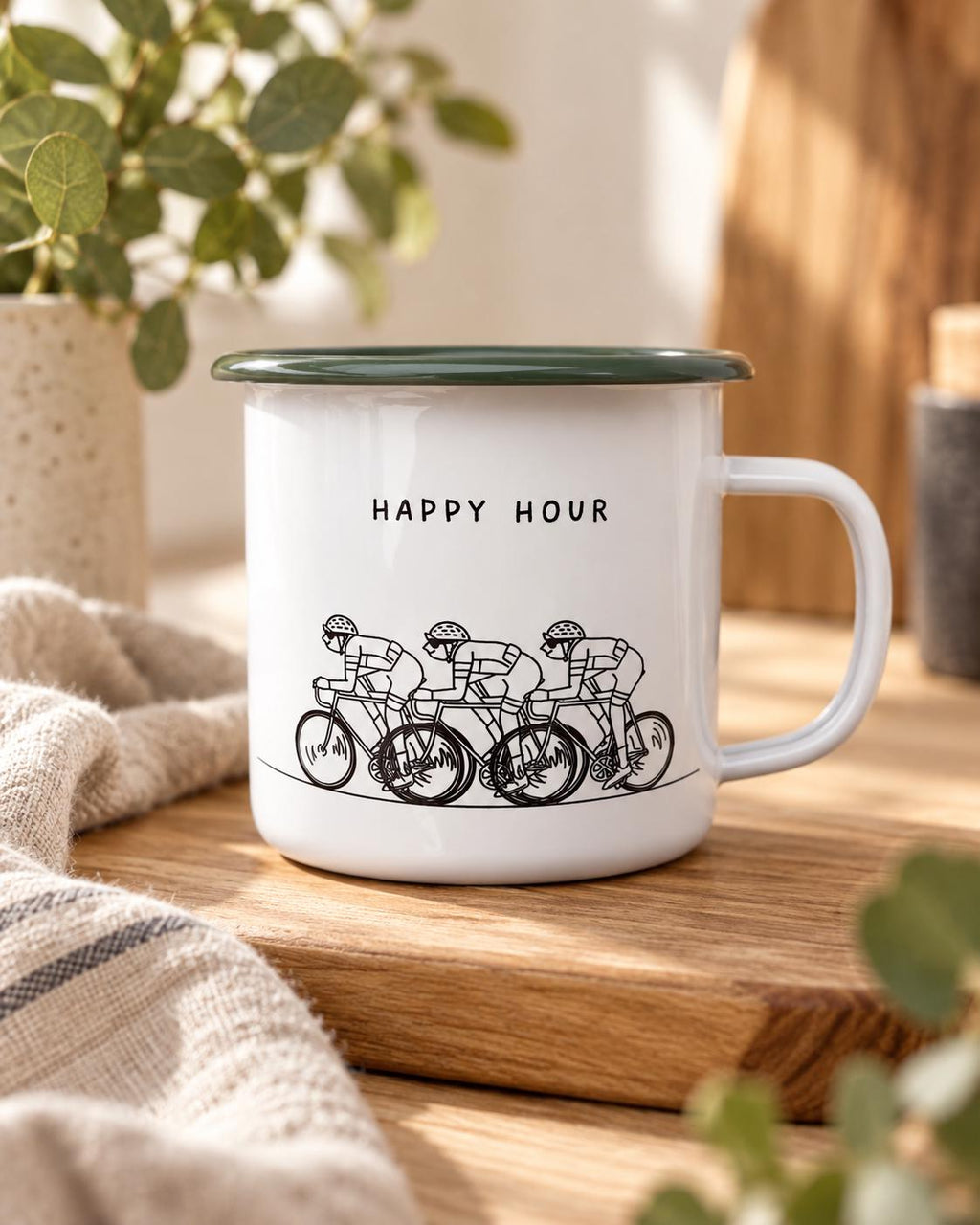A white enamel mug with a dark green rim and a handle. The front features a black line drawing of three cyclists riding in a row, positioned below the black text "HAPPY HOUR" printed in a simple, sans-serif font on the mug surface.