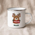 A white enamel mug with a silver metal rim displays a reindeer illustration with the name Noah on a beige linen background.