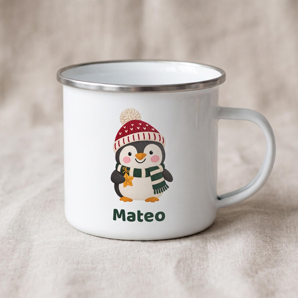 A white enamel mug with a silver metal rim shows a penguin wearing a winter hat and scarf with the name Mateo.