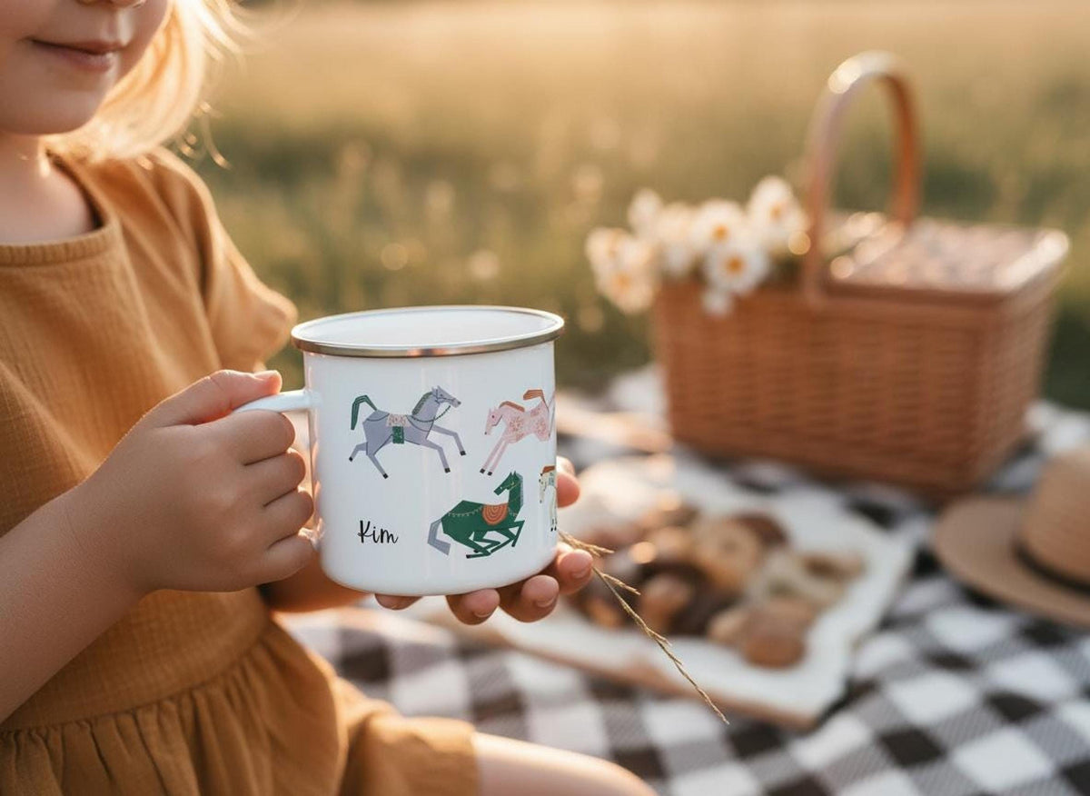 A child wearing an orange-brown dress holds a personalised white enamel mug with horse prints during a picnic on a black-and-white checkered blanket.