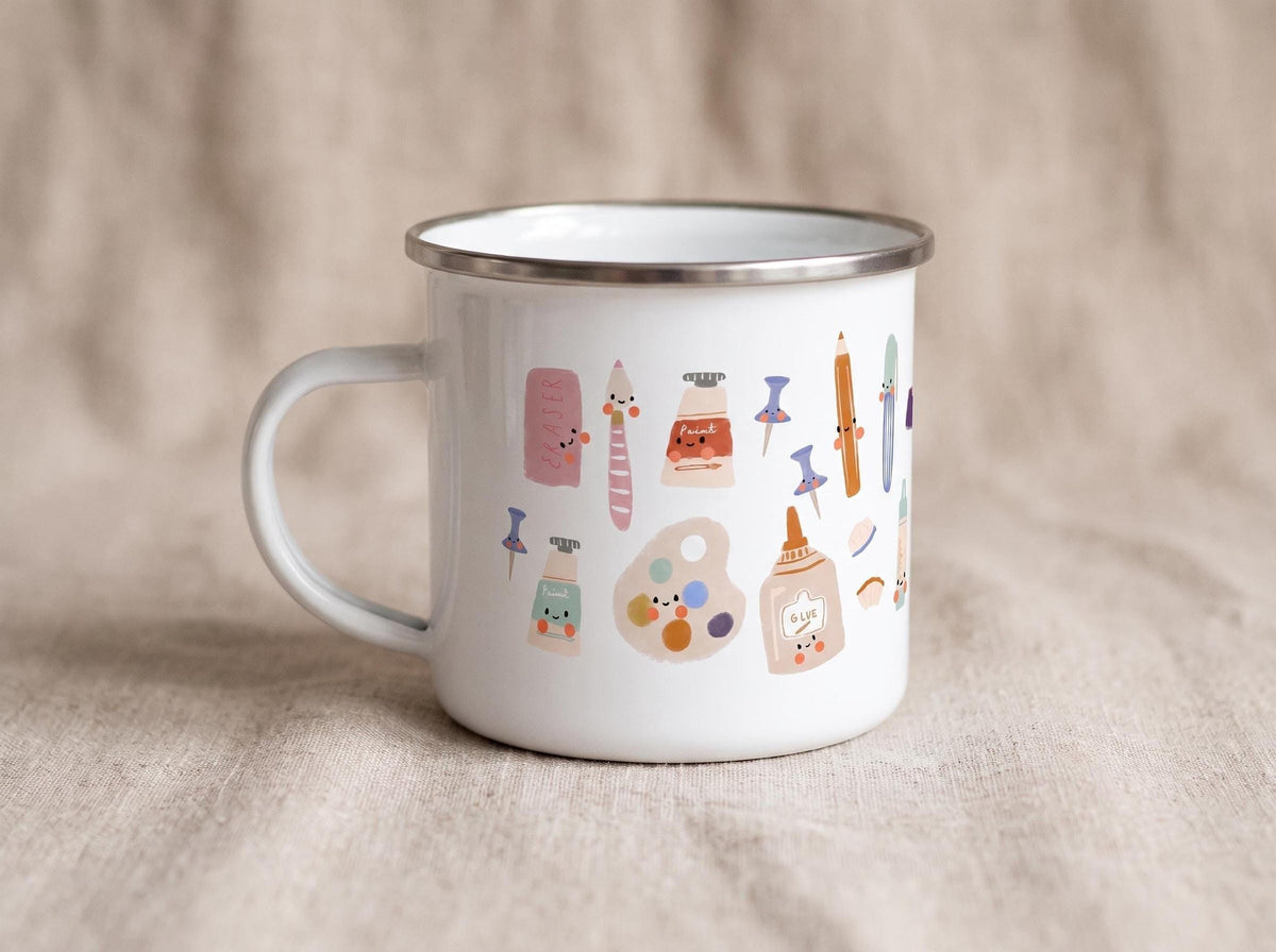 A white enamel mug with a silver rim and handle displays colourful illustrations of cute school supplies including an eraser, paint tube, and crayons.